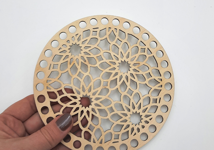 Hand holding a wooden coaster with intricate cut-out design on a white background