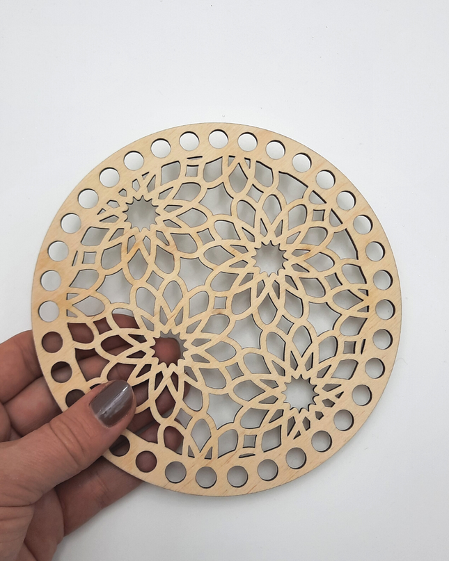 Hand holding a wooden coaster with intricate cut-out design on a white background